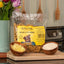 Bag of Betty Miller Cheese Little Bones dog food on a wooden surface with bowls of ingredients and flowers.