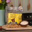 Bag of Betty Miller Everyday Liver Bones dog treats on a wooden surface with a bowl of treats and flowers in the background.