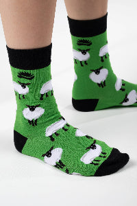 A pair of green and black bamboo socks with a sheep design, worn on a person's feet.