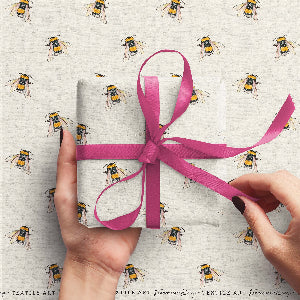 Gift wrapped in paper with bee pattern and pink ribbon, held by hands against matching background.